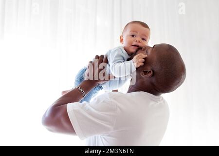 Il papà nero afro-americano bacia, tiene le braccia e ama il bambino di razza mista bambino su sfondo bianco Foto Stock