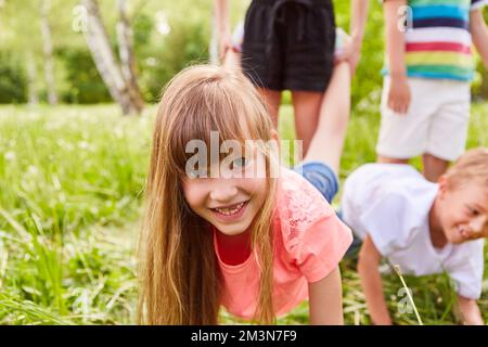 Ritratto di ragazza felice che gioca con gli amici durante la gara di carriola in giardino Foto Stock