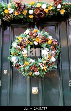 Natale corona di abete rosso con coni di pino bastoni di cannella e decorazioni a fette arancioni appesi alla porta verde Londra Inghilterra UK KATHY DEWITT Foto Stock