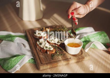 Donna che versa miele su gustoso panino di formaggio sul tavolo con luce e ombra Foto Stock