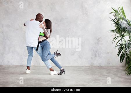 A lunghezza intera coppia multietnica balli latina, salsa o bachata in studio, parete sfondo chiaro Foto Stock