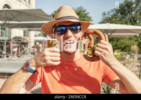 Ragazza con un bicchiere di birra e un tradizionale pretzel tedesco snack in biergarten o bar all'aperto Foto Stock