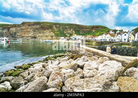 I visitatori si rilassano guardando verso sud attraverso Staithes Beck (fiume) presso il porto di Staiths presso il pittoresco villaggio di pescatori di Staithes. North Yorks Foto Stock