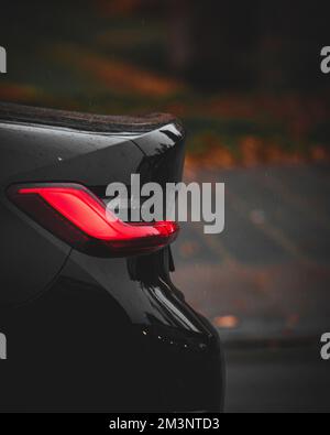 Immagine verticale delle luci posteriori di un'auto sportiva nera su sfondo sfocato Foto Stock