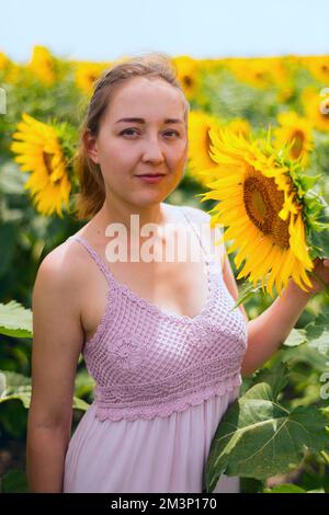 Bella ragazza giovane godendo la natura sul campo di girasoli al tramonto Foto Stock