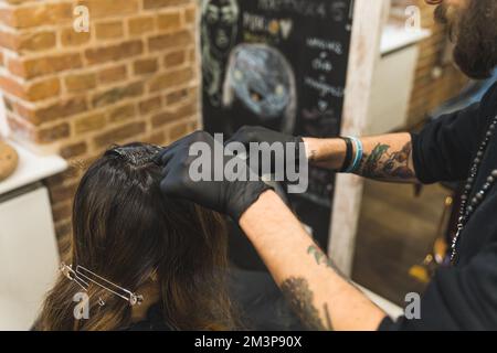 Parrucchiere con barba indossando guanti neri che tingano i capelli lunghi del suo cliente nel salone professionale dei capelli. Foto di alta qualità Foto Stock