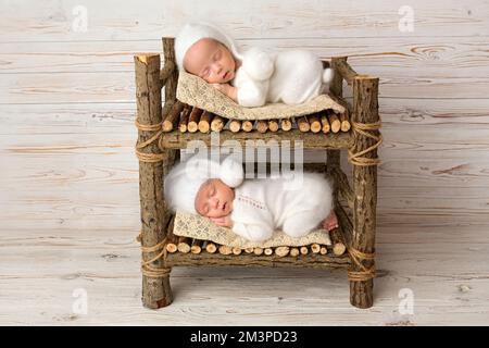 Piccoli neonati gemelli in tute bianche su sfondo di legno chiaro. Foto Stock