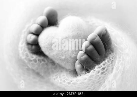 Piedi di un neonato con un cuore di legno, avvolto in una morbida coperta. Foto Stock