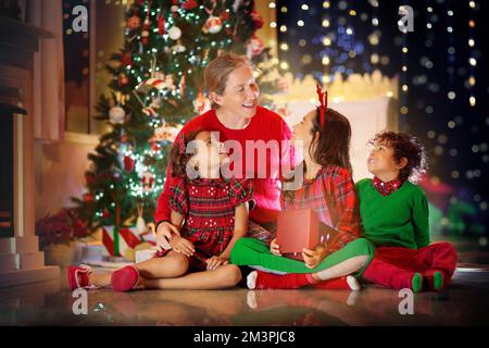 Famiglia sotto un albero di Natale. Madre e bambini con regali in soggiorno decorato con camino. Festa di Natale con a casa. Bambino con regali Foto Stock