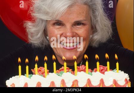 Donna più vecchia dai capelli grigi che si prepara a soffiare le candele sulla sua torta di compleanno Foto Stock