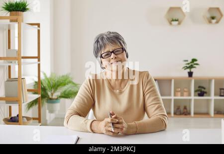 Donna anziana amichevole conduce consultazioni o lezioni online tramite webcam e video online. Foto Stock