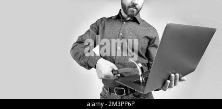 Uomo non rasato vista ritagliata rompere laptop colpire il computer con sfondo grigio martello, danni hardware. Foto Stock
