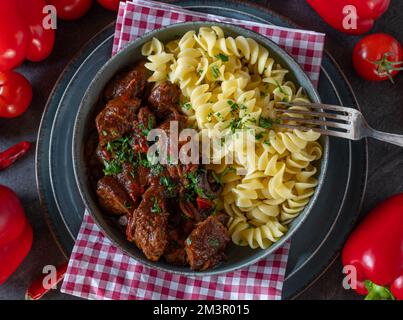 Gulasch ungherese con pasta imburrata su tavola scura. Giacitura piatta Foto Stock