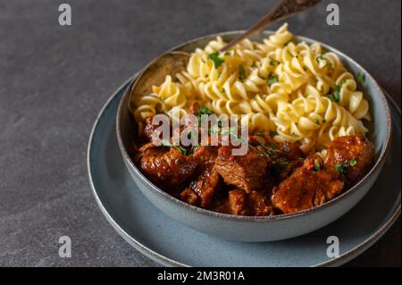 Gulasch ungherese con pasta in una ciotola isolata su fondo tavolo scuro. Foto Stock