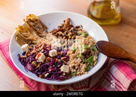 vista sul piatto di legno della ciotola vegetariana invernale con cavolo rosso, funghi, tofu, cereali farro, indivia e radicchio. Esempio di mare d'inverno o d'autunno Foto Stock