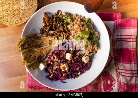 vista sul piatto di legno della ciotola vegetariana invernale con cavolo rosso, funghi, tofu, cereali farro, indivia e radicchio. Esempio di mare d'inverno o d'autunno Foto Stock