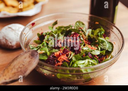 sana insalata invernale con barbabietola rossa, rucola di carote e insalata verde in ciotola di vetro su tavolo di legno Foto Stock