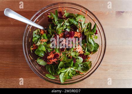 sana insalata invernale con barbabietola rossa, rucola di carote e insalata verde in ciotola di vetro su tavolo di legno Foto Stock