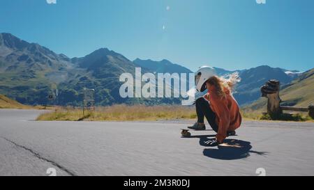 Sessione cinematografica di longboard in discesa. Giovane donna skateboard e fare trucchi tra le curve su un passo di montagna. Concetto di sport estremi Foto Stock