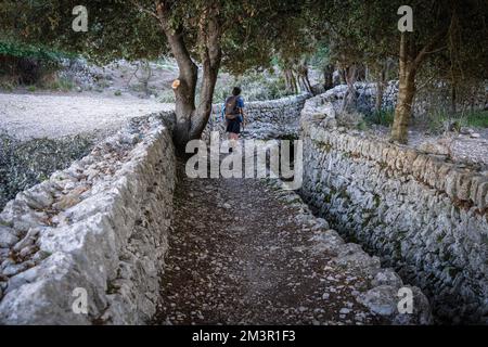 Escursionisti a piedi tra le mura di pietra vicino a un fossato tradizionale, Oriente , Bunyola, Maiorca, Isole Baleari, Spagna Foto Stock