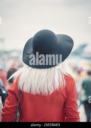 Vista posteriore con una donna non identificata in un cappotto rosso e con un grande cappello nero sulla testa. Foto Stock