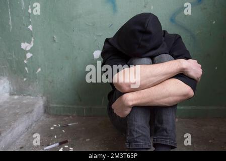 Un tossicodipendente adolescente si siede da solo dopo aver usato droghe e alcol in una casa abbandonata. Concetto di dipendenza Foto Stock