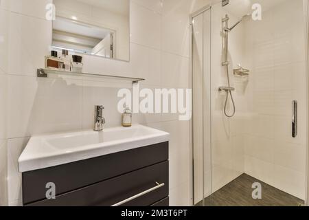 un bagno moderno con piastrelle bianche e nere alle pareti, lavandino, specchio e box doccia nell'angolo Foto Stock