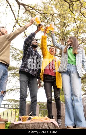 Quattro persone che hanno una birra insieme, festival tradizionale della birra, gruppo di corse miste di amici e coppie che si divertono all'aperto Foto Stock