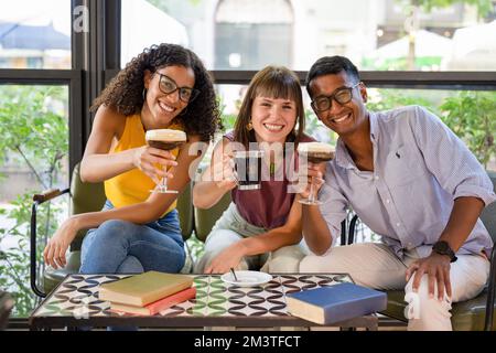 Gruppo di amici sorridenti e seduti in una caffetteria, giovani che hanno caffè e allegria Foto Stock