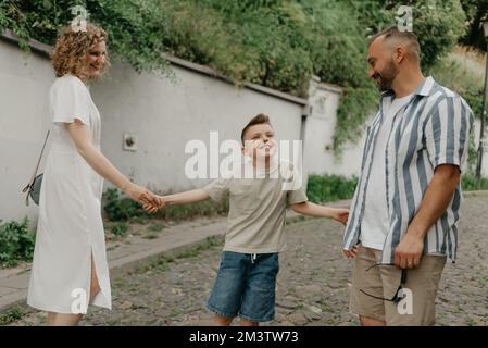 Padre, madre e figlio stanno tenendo le mani sulla strada acciottolata verde Foto Stock