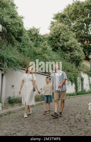 Padre, madre e figlio stanno tenendo le mani sulla strada acciottolata verde Foto Stock