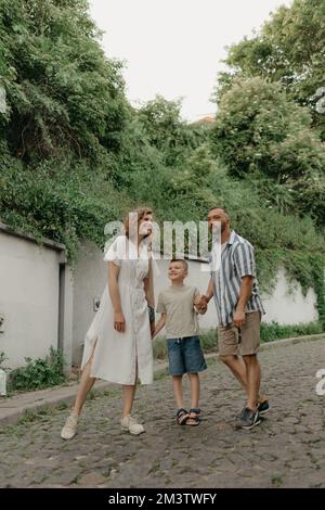 Padre, madre e figlio stanno tenendo le mani sulla strada acciottolata verde Foto Stock