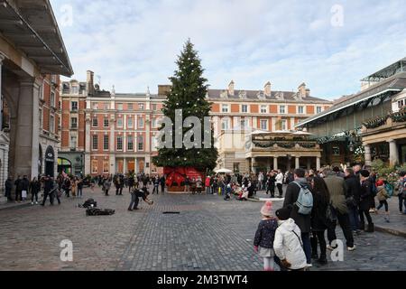 Vista dell'albero di Natale di Covent Garden e di un Street performer che intrattiene il pubblico, Covent Garden, Londra, Regno Unito. Foto Stock