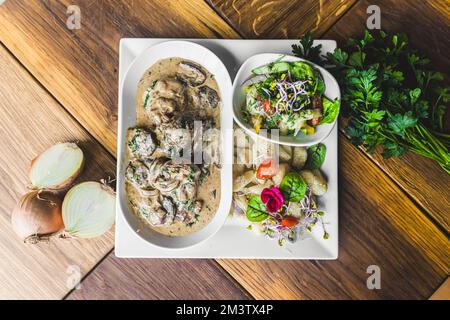 Shot ad angolo alto di gustosa sirloin in salsa di funghi spessi servito su piatto bianco con gnocchi di patate e insalata. Concetto di nutrizione. Foto di alta qualità Foto Stock