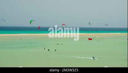 Gruppo di kitesurf kiteboarding sulle onde dell'Oceano Atlantico a Playa Esmeralda, Fuerteventura, Isole Canarie, Spagna. Azure calmo oceano onde Foto Stock