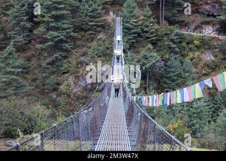 Everest base Camp Trek - 18 ottobre 2015: I portieri nepalesi trasportano merci sul ponte sospeso. Foto Stock