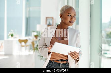 Chissà a cosa porterà la mia prossima mossa. una giovane donna d'affari che usa un tablet digitale mentre guarda fuori dalla finestra in un ufficio. Foto Stock