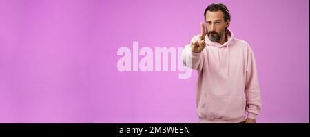 Una regola per ascoltare. Serio-osservante Bossy messo a fuoco determinato adulto sopportato maschio in felpa rosa estende l'indice del dito primo numero che scolding fa l'affermazione Foto Stock