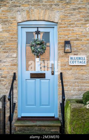 Corona di Natale su una porta di un cottage in pietra. Riposto sul Wold, Cotswolds, Gloucestershire, Inghilterra Foto Stock