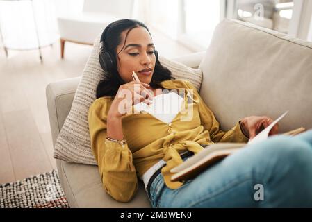 La musica mi aiuta a concentrarmi sul mio lavoro. una giovane e attraente donna d'affari sdraiata sul divano e ascoltando musica mentre scriveva appunti. Foto Stock