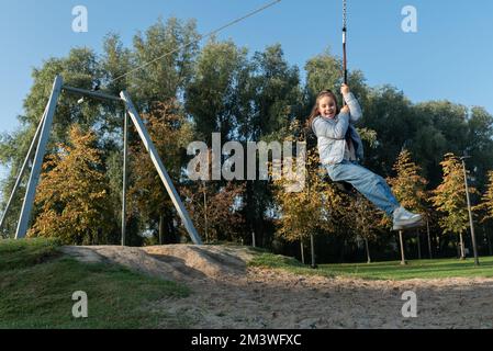 Ricreazione autunnale in natura. Giovane ragazza in sella a un bungee appeso sul parco giochi. Foto Stock