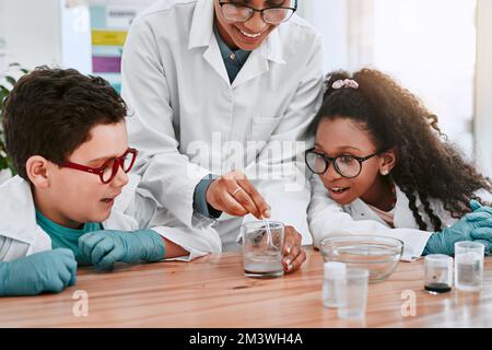 Theyre sempre desideroso di imparare le cose nuove. due adorabili giovani allievi della scuola che fanno un esperimento con il loro insegnante di scienza a scuola. Foto Stock