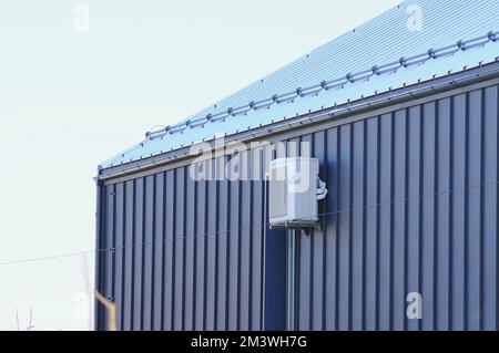 Un condizionatore d'aria esterno sulla facciata della casa in inverno. La facciata di rivestimento in metallo è nera Foto Stock