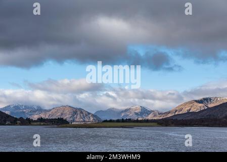 Splendida vista sul paesaggio invernale lungo Loch Leven passato Ballachulish Bridge verso le montagne innevate in lontananza con il cielo suggestivo Foto Stock