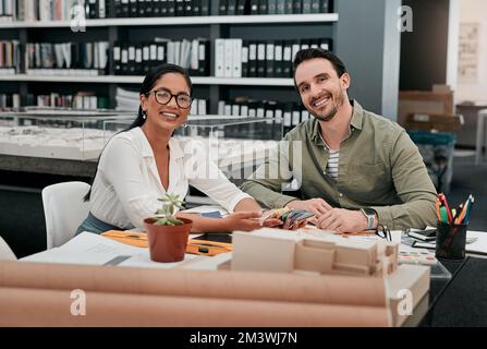 Lavoriamo meglio insieme. Ritratto corto di due aspiranti giovani architetti sorridenti mentre lavorano insieme in un ufficio moderno. Foto Stock