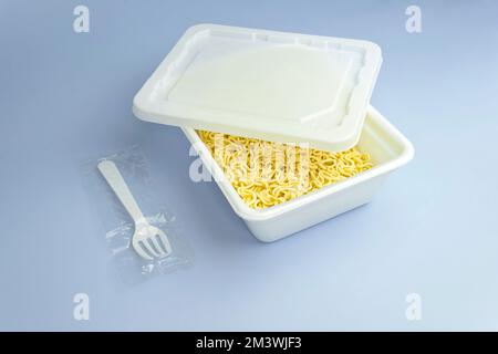 Spaghetti secchi istantanei in scatola di plastica sul tavolo blu Foto Stock