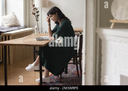 Donna stanca seduta a un tavolo con un computer portatile in ufficio a casa Foto Stock