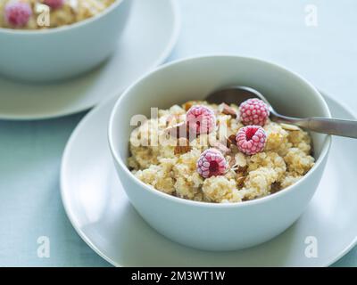 Porrige in quinoa sul tavolo. Due ciotole con porridge di latte di quinoa con frutti di bosco e mandorla. Lamponi congelati in porrige di quinoa Foto Stock
