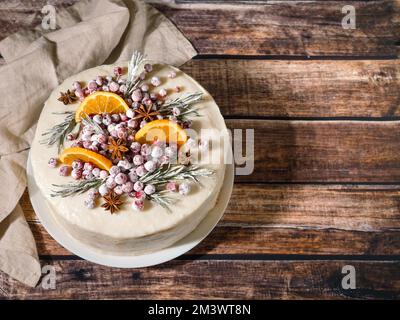 Torta invernale fatta in casa su sfondo di legno. Panna bianca torta di natale al rosmarino, mirtilli, anice stellato e fette di arance. Spazio di copia. Vista dall'alto Foto Stock