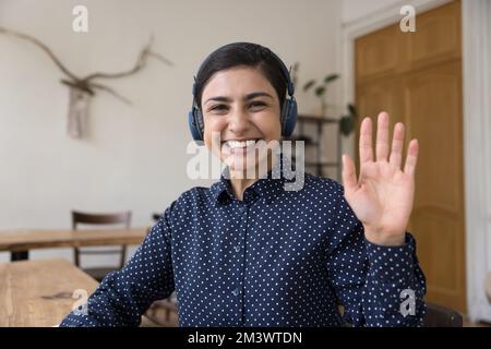 Felice bella donna indiana in cuffie wireless che sventola il ciao mano Foto Stock